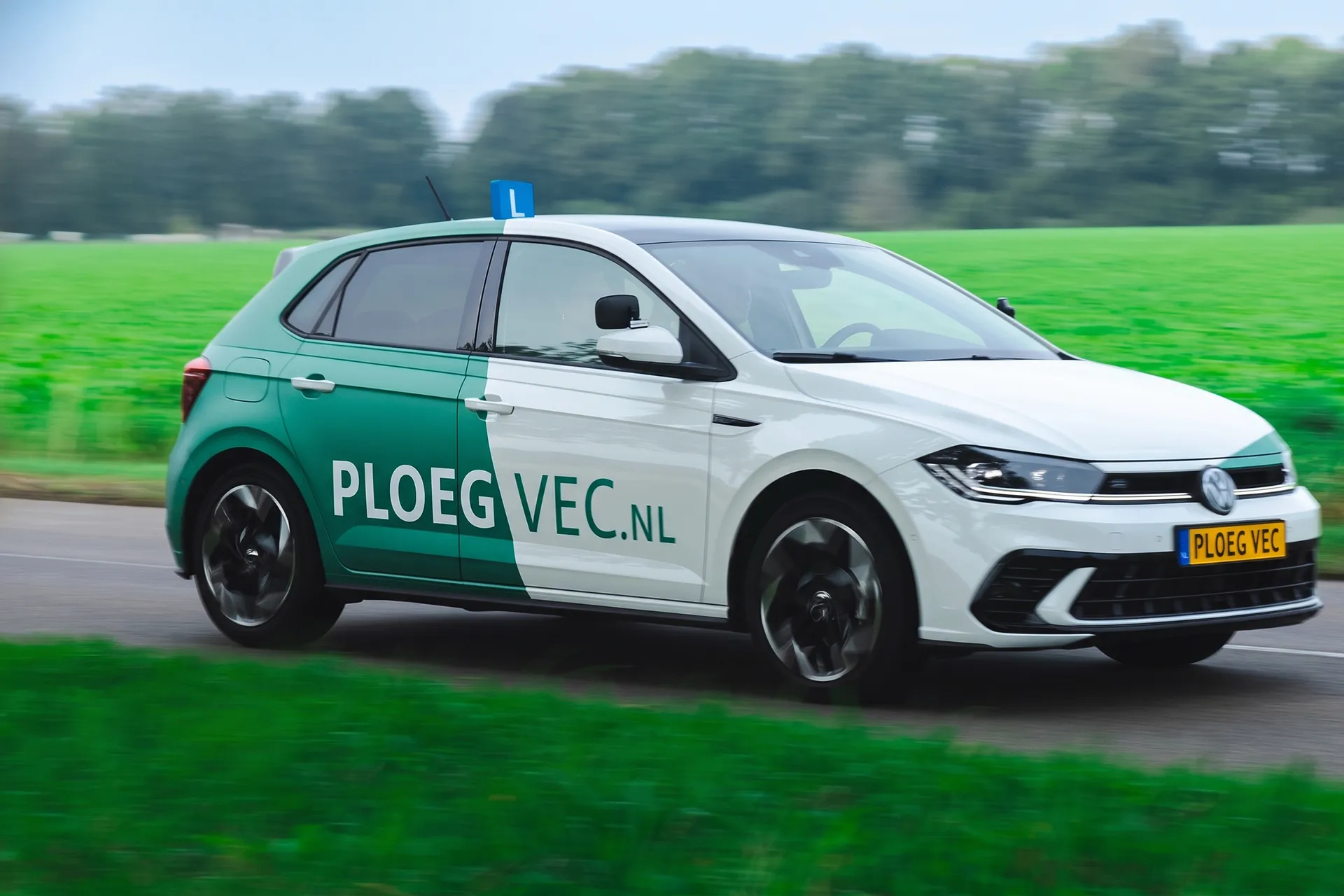 Rijdende lesauto met groene en witte bekleding op een landelijke weg.
